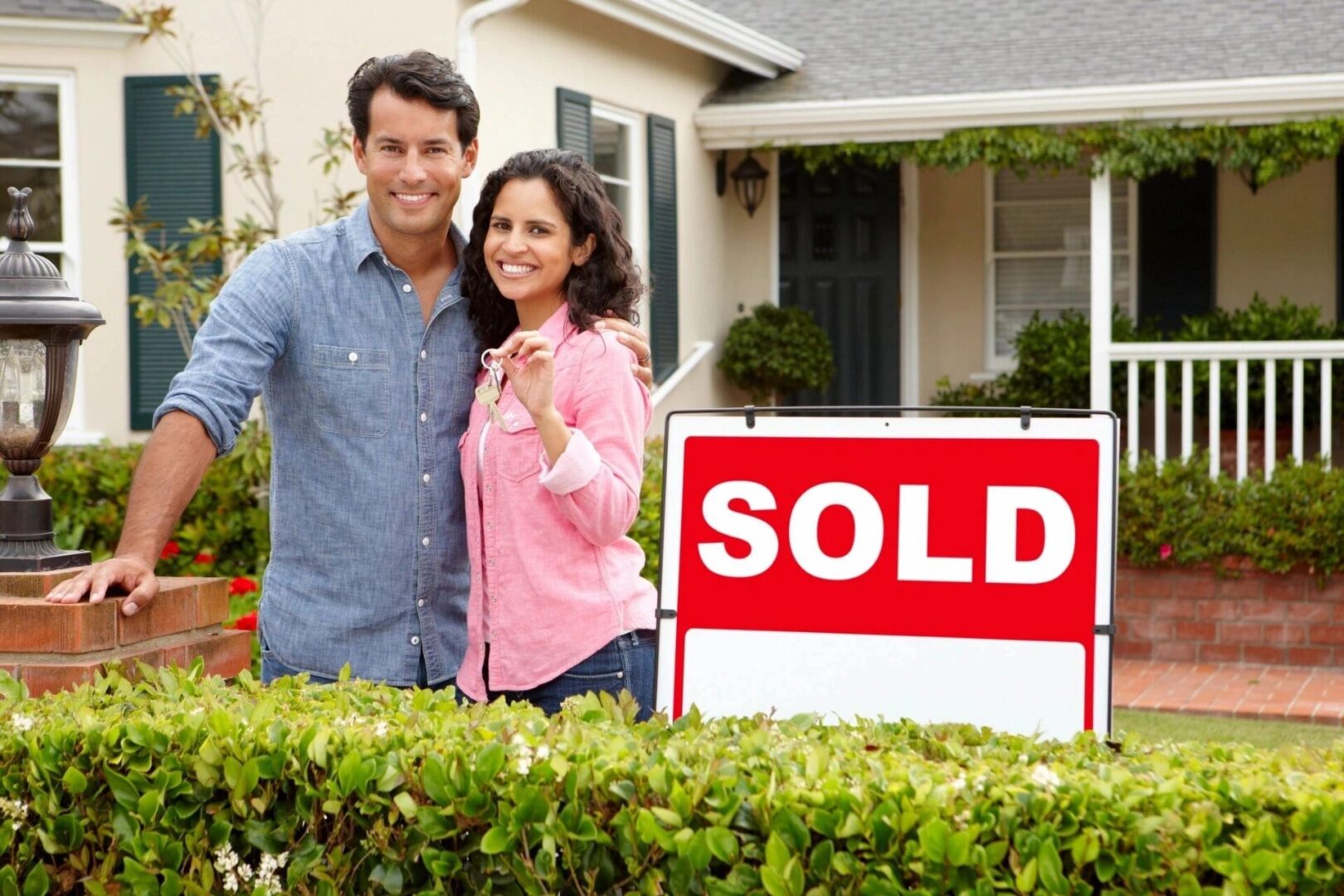 A couple standing in front of their home with keys.